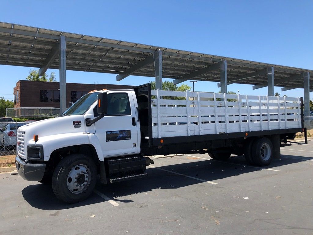 A white GMC C6500 diesel commercial truck with a life gate truck body in the parking lot.